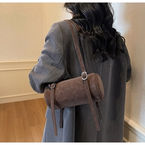 Detail of dark brown cylinder bag with adjustable straps and matte leather finish