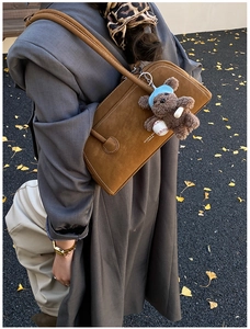 Detail view of brown matte leather shoulder bag with plush bear charm on autumn background