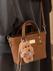 Brown leather tote bag with plush dog charm worn by a model in a dark coat