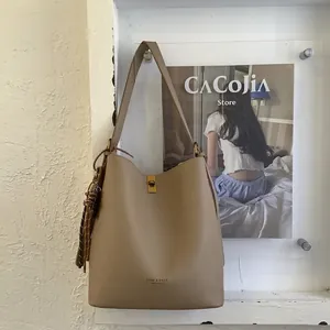 Détail du sac seau beige à motif litchi avec boucle dorée et pendentif à pompon tressé