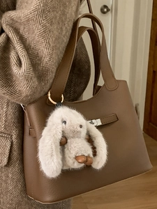 Minimalist brown leather bucket bag with plush rabbit charm and turn-lock closure