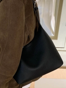 Minimalist black lychee pattern leather bucket bag with silver buckle worn by a model