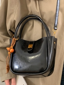 Sac seau noir brillant avec boucle dorée et charm en perles sur un trench-coat