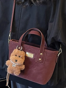Fashionable burgundy tote bag with plush puppy charm shown from a side perspective