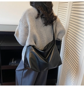 Detailed view of the black matte leather large shoulder bag worn by a model in a minimal room