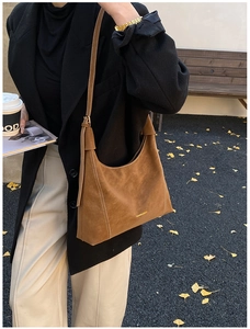 Close-up of brown suede hobo bag with gold logo and white contrast stitching detail
