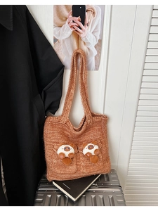 Detail of red-brown knit tote bag showing thick texture and cute plush cat pocket ornaments