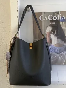 Sac seau minimaliste en cuir noir grainé avec fermoir doré et pendentif ours