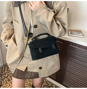 Detail view of a vintage black leather crossbody bag with dual buckle straps and top handle