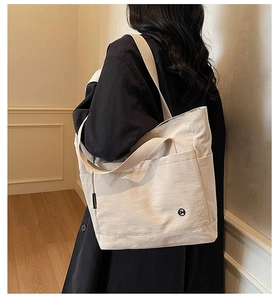 Detail view of a beige high-capacity tote bag with side pockets on a black coat