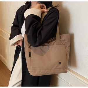 Detailed side view of khaki tote bag featuring woven brand label and outer pocket detail