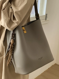 Sac seau gris en cuir avec boucle dorée et pompon tissé pour un style minimaliste élégant