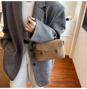 Detail of vintage brown textured leather handbag with gold buckles on a grey blazer