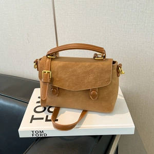 Detail view of brown faux suede handbag with gold hardware on a white prop book
