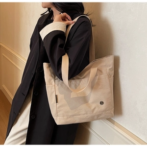 Detail of beige canvas tote bag with side pocket and shoulder strap on model in black coat