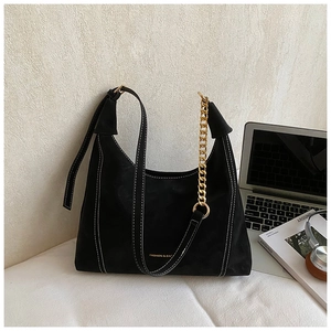 Detail of black suede tote bag featuring contrast white stitching and gold chain accents