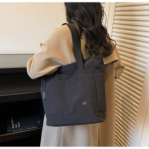 Detail of black canvas tote bag with side strap and brand logo in a lifestyle setting