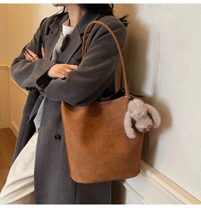 Detail of brown woven faux leather tote bag with a soft grey plush rabbit keychain charm