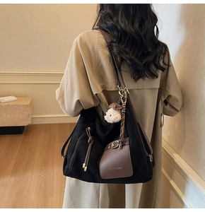 Détail d'un sac cabas en daim noir avec bordure en cuir marron et breloque chiot