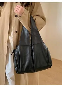 Détail d'un grand sac cabas en cuir ciré noir porté avec un trench-coat kaki chic