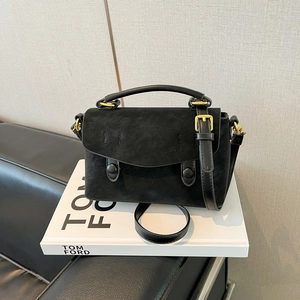 Detail view of black suede crossbody bag with gold hardware on a decorative book