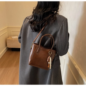 Détail du sac seau en cuir marron avec perles décoratives et logo vintage embossé
