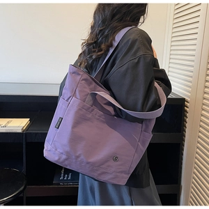 Detail view of large purple canvas tote bag with metal logo on casual urban lifestyle setting