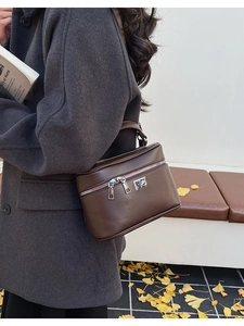 Detail view of brown leather box bag with dual silver zippers and metal turn lock