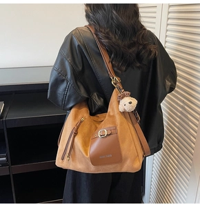 Détail d'un grand sac cabas en daim marron avec poche à boucle et pompon sur la fermeture