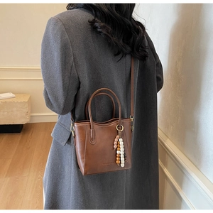 Détail d'un sac seau vintage marron avec pompon en perles et logo embossé élégant
