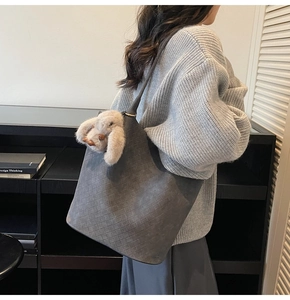 Detail of grey woven tote bag with brown plush bunny charm on female model