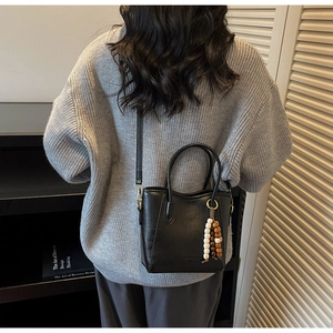 Vue lifestyle d'un sac seau noir avec perles en bois porté sur un pull gris élégant