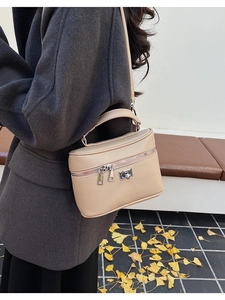 Close-up of beige leather box bag with silver zippers and handle in a winter street setting