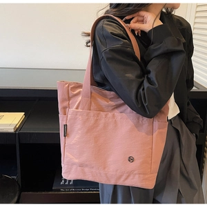 Detail of a large pink tote bag with brand label and metallic logo on nylon fabric