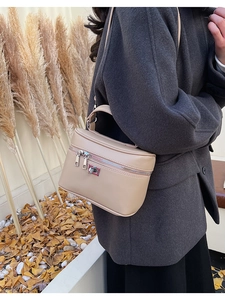 Detail of beige leather box handbag featuring dual zippers and silver metallic buckle