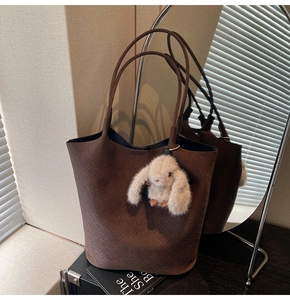 Detail of a brown woven tote bag with Intrecciato pattern and white bunny charm accessory