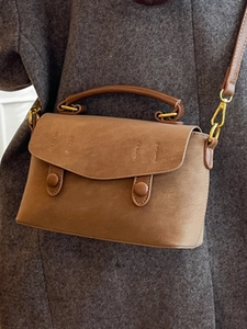 Minimalist brown crossbody bag with handle and gold hooks on a grey wool coat