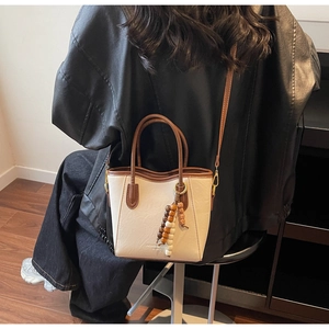 Détail du sac seau crème avec bordure en cuir marron et pendentif à pampilles