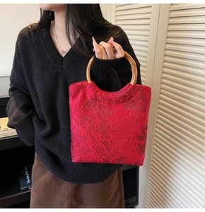 Detail of red floral brocade tote bag with vintage bamboo handles on a black sweater