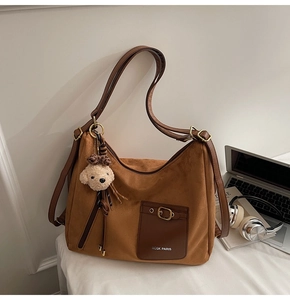 Détail d'un sac hobo en daim marron avec une poche en cuir et un charmant porte-clés ours