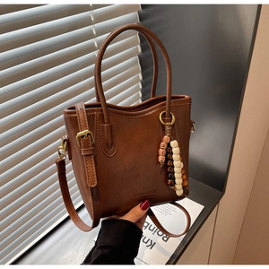 Vue détaillée du sac seau marron avec logo de mode et pompon en perles boisées