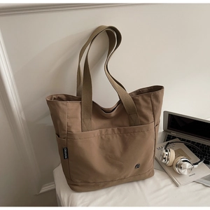 Detail of tan canvas tote bag with large front pocket and side compartments on desk