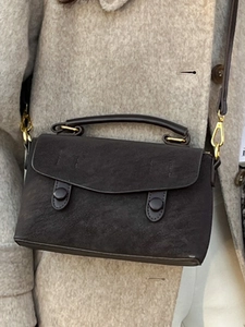 Minimalist dark grey frosted crossbody bag with top handle and gold hardware on beige coat