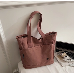 Close-up of pink tote bag with front pocket and side label in a cozy desk setting