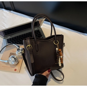 Détail du sac seau en cuir marron foncé avec pendentif en perles de bois et logo