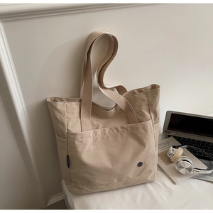 Detail of minimalist beige canvas tote bag showing front pockets and dual straps design
