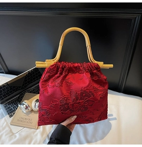 Detail of red satin tote with floral embroidery and natural bamboo handle in a home setting