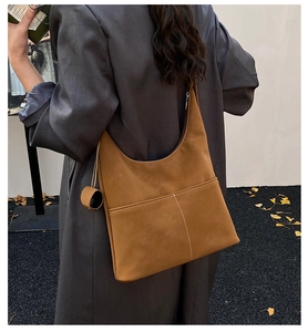 Close-up of caramel faux leather hobo bag with stitched front pocket and side charm detail