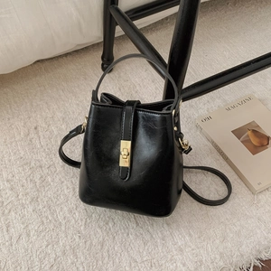 Vue de dessus d'un sac seau en cuir noir avec fermoir doré sur un tapis blanc et un magazine