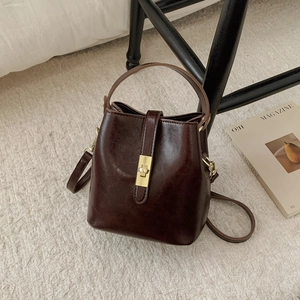 Détail du sac seau rétro en cuir ciré avec fermoir doré sur un tapis beige moelleux